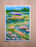 Framed painting of a colorful floral landscape on a wooden table.